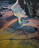 Luftaufnahme von Gletscherflüssen, die sich durch vulkanischen Sand schlängeln und die Landschaft in ätherische Blau-, Orange- und Violetttöne tauchen, Hvolsvllur, Südregion, Island.