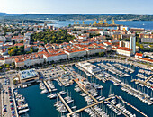 Luftaufnahme von glitzernden Booten, die den Jachthafen füllen, im Kontrast zu den orangefarbenen Dächern und der dahinter liegenden Adria, Triest, Friaul-Julisch-Venetien, Italien.