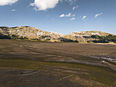 Luftaufnahme von zerklüfteten Bergen, die auf die weite, sonnendurchflutete Hochebene von Campo Imperatore treffen, ein Tanz von Licht und Schatten in der italienischen Landschaft, Gran Sasso, Abruzzen, Italien.