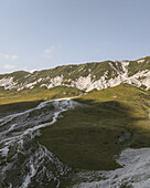Luftaufnahme der zerklüfteten, sonnenverwöhnten Hügel des Campo Imperatore, ein Teppich aus grünen Wiesen und weißen Felsformationen unter einem ruhigen Himmel, Gran Sasso, Abruzzen, Italien.