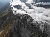 Luftaufnahme von Wolken, die um die felsigen Gipfel des Campo Imperatore wirbeln und Schatten auf das zerklüftete Terrain werfen, Gran Sasso, Abruzzen, Italien.