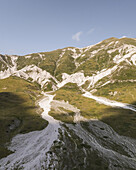 Luftaufnahme von weißen Felsformationen inmitten grüner Hänge unter einem blauen Himmel in Campo Imperatore, Gran Sasso, Abruzzen, Italien.