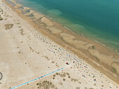 Aerial view of turquoise waters edge the sandy beach where people bask under the sun, Bernières-sur-Mer, Normandy, France.