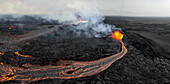 Luftaufnahme von feurigen Flüssen aus geschmolzener Lava, die sich ihren Weg durch die kahle, schwarze, in Rauch gehüllte Vulkanlandschaft bahnen, Grindavik, Grindav?kurb?r, Island.