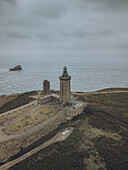 Aerial view of the imposing Cap Fréhel lighthouse stands proudly against the moody, grey Atlantic, its stone walls weathered by time and sea spray, Plévenon, Bretagne, France.