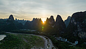 Aerial view of the Karst Mountains with the sun setting behind the peaks and a river flowing through the landscape, Yangshuo, China.