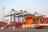 Middle East, Middle East - 19 December 2023: View of towering cranes against a pastel sky dwarf stacks of vibrant shipping containers in a busy port, hinting global trade.