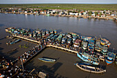 Aerial view of the bustling, vibrant riverfront market with fishing boats docked along the pier, a flurry of activity amidst the waters, Yanam, Puducherry, India.