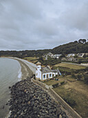 Aerial view of the Phare de Nantouar with a red-topped tower contrasts against the dark rocks and the beach, nestled by lush greenery, Louannec, Bretagne, France.