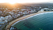 Luftaufnahme der Sonne, die die Küste küsst und goldene Farbtöne auf den Strand und das türkisfarbene Wasser malt, im Kontrast zur üppig grünen Landschaft, Terrigal, New South Wales, Australien.
