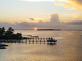 Aerial view of the sun setting over the tranquil waters, casting a golden glow on the docks and distant islands, creating a serene coastal vista, Key Largo, Florida, United States.