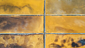 Aerial view of golden and ochre salt pans create a striking mosaic of earth tones, divided by stark white lines in the sun-drenched landscape, Pag, Zadar County, Croatia.