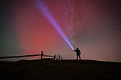 View of a lone figure standing on a hill, illuminating the vibrant, star-filled night sky with a beam of light, Gaberl, Styria, Austria.