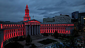 Luftaufnahme des Denver City and County Building, das in der Dämmerung in einem kräftigen Rot leuchtet, Denver, Colorado, Vereinigte Staaten.