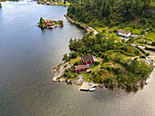 Aerial view of houses perched on rocky outcrops amidst the shimmering waters, a tranquil escape under the vast sky, Sogne, Agder, Norway.