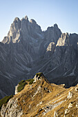 Blick auf schroffe, sonnenbeschienene Gipfel, die in den klaren Himmel ragen und im Kontrast zu den goldenen Farbtönen des grasbewachsenen Vordergrunds in Misurina, Belluno, Italien, stehen.
