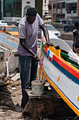 Dakar, Senegal - 12 May 2025: View of a craftsman's hands, painting vibrant colors onto a traditional boat at Plage de Soumbédioune, reflecting the lively spirit of the city.