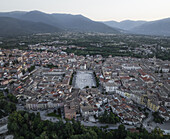 Luftaufnahme der historischen Piazza Garibaldi, deren heller Stein mit den umliegenden Terrakotta-Dächern kontrastiert, eingebettet in üppiges Grün und hoch aufragende Berge, Sulmona, Abruzzen, Italien.