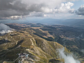 Luftaufnahme von zerklüfteten Bergen unter einem dramatischen Himmel, wo Schatten über die Gipfel in der Nähe von Campo Imperatore, Gran Sasso, Abruzzen, Italien tanzen.