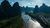 Aerial view of the Li River cutting through the soaring karst mountains, with boats gliding on the sunlit waters, Yangshuo, China.