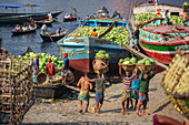 Dhaka, Bangladesh - 08 April 2023: View of bustling riverbank activity as laborers carry baskets of watermelons from boats, creating a vibrant scene of commerce and daily life.