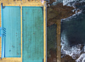 Luftaufnahme der kontrastreichen Blautöne der Newcastle Ocean Baths, die auf die zerklüftete, von Wellen umspülte Küstenlinie treffen, eine Symphonie aus Natur und menschlicher Gestaltung, Newcastle, New South Wales, Australien.
