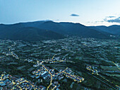 Aerial view of the quiet town nestled amongst the mountains, with the lights twinkling softly against the dark green landscape, Sulmona, Abruzzo, Italy.
