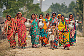 Bogura, Bangladesh - 13 December 2019: View of village women, adorned in vibrant saris, carry gleaming water pots along a dusty path, their faces etched with resilience and community spirit.