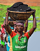 Dhaka, Bangladesh - 17 March 2017: View of a man carrying a heavy load of dark coal in a woven basket atop his head, a testament to labor and resilience.