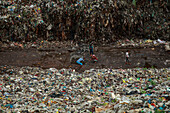 Chattogram, Bangladesch - 05. Oktober 2020: Blick auf Kinder, die durch eine weite Landschaft aus weggeworfenen Abfällen navigieren, die in starkem Kontrast zum Himmel stehen.