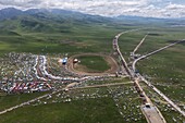 Aerial view of a vibrant horse festival ground with a race track, bustling with activity and colorful tents against the green meadow, Horse Festival, Sichuan, China.