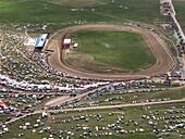 Aerial view of a vibrant horse festival ground with a race track, bustling with activity and colorful tents against the green meadow, Horse Festival, Sichuan, China.