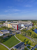 Orlando, United States - 21 July 2025: Aerial view of Camping World Stadium basking under a clear sky, its vibrant red and yellow accents standing out against the lush green landscape.