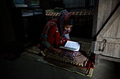 Mirsharai, Bangladesh - 07 May 2020: View of a young girl in a red patterned salwar kameez, deeply engrossed in reading a book on a mat indoors.
