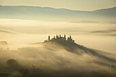 View of a Tuscan villa perched atop a hill shrouded in a mystical fog, bathed in the soft, golden light of dawn, creating a serene landscape, San Quirico d'Orcia, Tuscany, Italy.