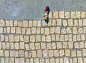 Bogura, Bangladesh - 23 March 2023: Aerial view of a woman in vibrant attire amidst the geometric patterns of drying food, creating a striking contrast against the concrete.