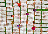Bogura, Bangladesh - 04 May 2023: Aerial view of women in vibrant saris amidst a grid of drying rice cakes, creating a mosaic of color and texture under the open sky.