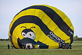 Chambley, France - 30 July 2025: View of a vibrant yellow and black hot air balloon, resembling a giant bumblebee, rests on the green field at Aérodrome de Chambley.