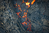 Luftaufnahme von geschmolzener Lava, die sich durch die zerklüftete, geschwärzte Erde in der Nähe von Reykjanes schlängelt. Die intensive Hitze kontrastiert mit dem kühlen vulkanischen Gestein, Grindavik, Grindav?kurb?r, Island.