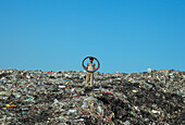 Chattogram, Bangladesh - 03 November 2019: View of a young boy standing atop a landfill, holding a tire against a backdrop of clear blue skies.