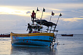 Chattogram, Bangladesh - 19 September 2023: View of a weathered fishing boat adorned with Bangladeshi flags sits stranded on a shimmering, muddy shore, under a pastel sky.