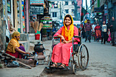 Bogura, Bangladesh - 17 December 2019: View of a smiling woman in a wheelchair amidst the bustling street scene, where vibrant colors meet the rustic charm of local life.