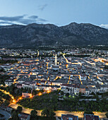 Aerial view of a sprawling town nestled against the backdrop of majestic mountains, lights twinkling like stars in the early evening, Sulmona, Abruzzo, Italy.