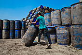 Narayanganj, Bangladesh - 27 February 2021: View of workers amidst towering stacks of weathered, blue plastic drums, a stark contrast against the clear sky.