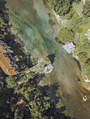 Aerial view of the bridge over the clear, turquoise river meeting the sandy shore, surrounded by lush green trees, Gorges du Tarn, Occitanie, France.