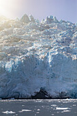 Blick auf eine kolossale, in eisigem Blau und Weiß schimmernde Gletscherwand, die über das dunkle, mit treibendem Eis übersäte Wasser der Aialik Bay ragt, Kenai Fjords National Park, Seward, Alaska, Vereinigte Staaten.
