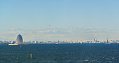 View of the futuristic, dome-shaped structure contrasting with the distant cityscape under a serene blue sky, reflected in the calm, Nakajima, Japan.