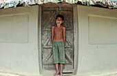 Mirsharai, Bangladesh - 21 October 2019: View of a joyful, shirtless boy with an infectious laugh standing against the textured, white wall of a simple dwelling.