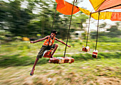 Bogura, Bangladesh - 15 March 2018: View of a young boy in mid-air on a swing, a blur of motion against the soft greens of the park.