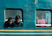 Chittagong, Bangladesch - 28. November 2019: Blick auf Kinder, die durch die verwitterten, türkisfarbenen Zugfenster schauen, ihre fröhlichen Gesichter bilden einen lebhaften Kontrast zum gealterten Metall...